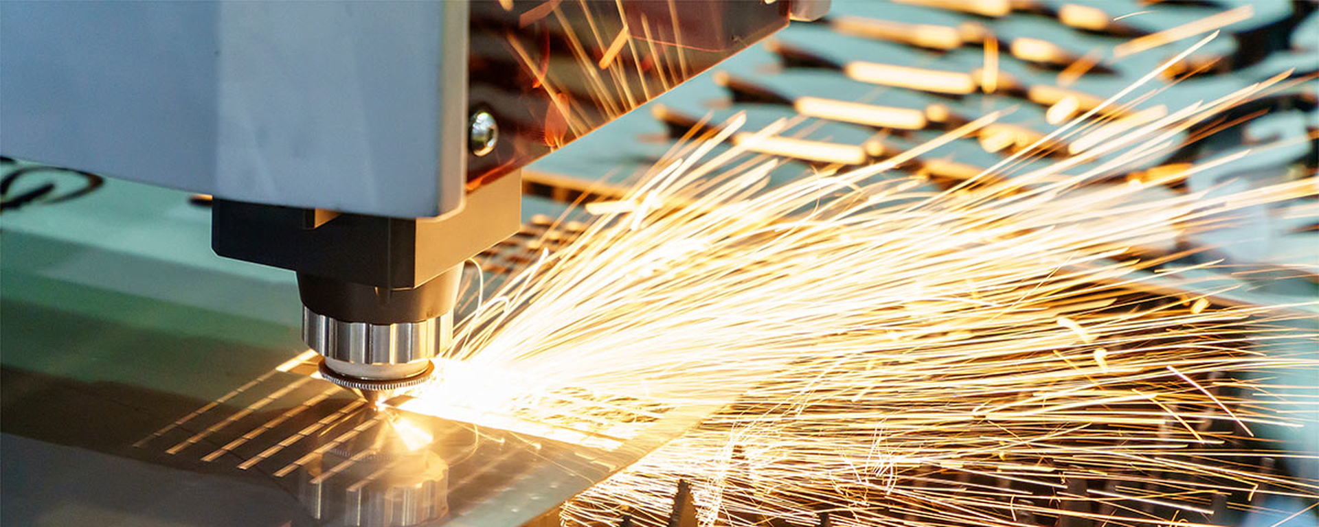 High-speed laser cutting machine generating bright sparks while cutting through a metal sheet.